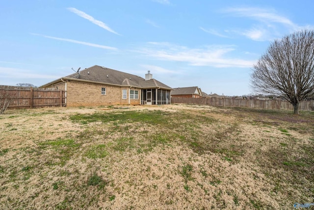 rear view of house with a fenced backyard, brick siding, a sunroom, a lawn, and a chimney