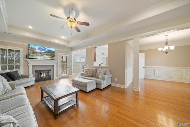 living room featuring light wood-style floors, a fireplace with flush hearth, a tray ceiling, and crown molding