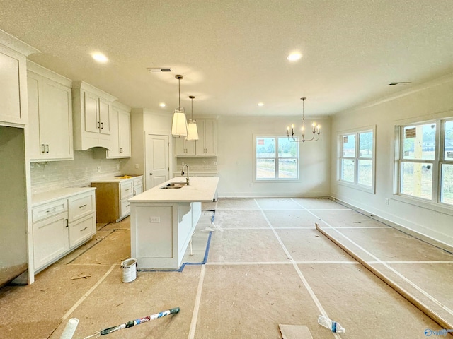 kitchen with white cabinets, hanging light fixtures, a kitchen island with sink, light countertops, and a sink