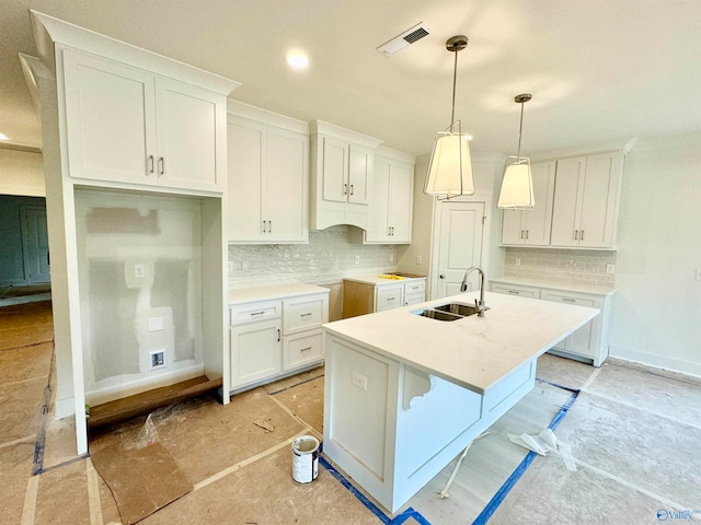 kitchen with decorative light fixtures, a sink, white cabinetry, light countertops, and a center island with sink