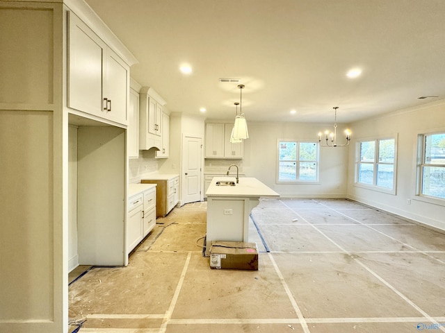 kitchen with a sink, white cabinets, light countertops, a center island with sink, and pendant lighting