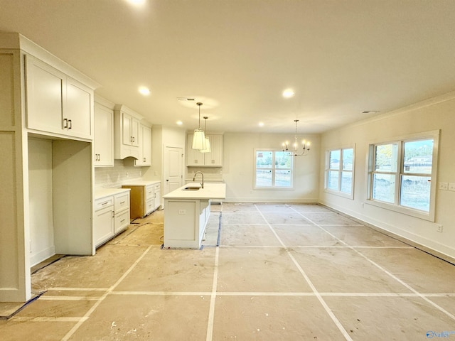 kitchen with a sink, white cabinetry, baseboards, light countertops, and a center island with sink