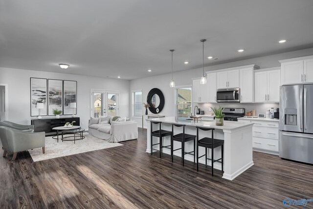 kitchen featuring appliances with stainless steel finishes, decorative light fixtures, an island with sink, and white cabinets