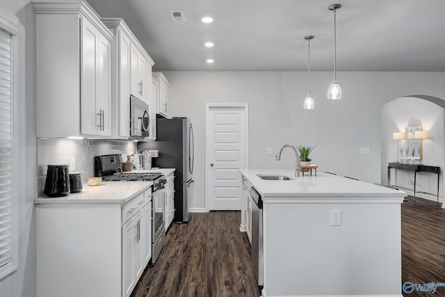 kitchen with sink, appliances with stainless steel finishes, white cabinetry, hanging light fixtures, and an island with sink