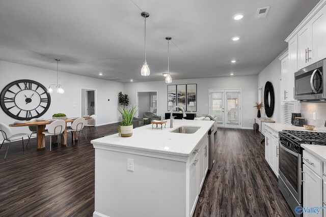 kitchen with appliances with stainless steel finishes, dark hardwood / wood-style flooring, white cabinetry, and an island with sink