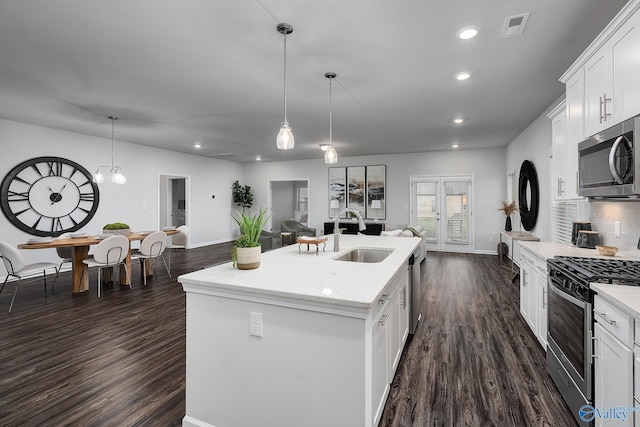 kitchen with sink, hanging light fixtures, stainless steel appliances, white cabinets, and a center island with sink