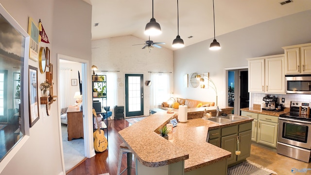 kitchen with sink, appliances with stainless steel finishes, a kitchen island with sink, a kitchen bar, and decorative light fixtures