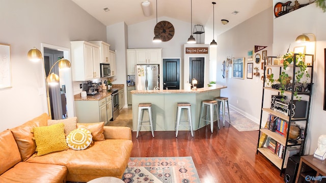 kitchen with a breakfast bar, hanging light fixtures, stainless steel appliances, white cabinets, and a center island with sink