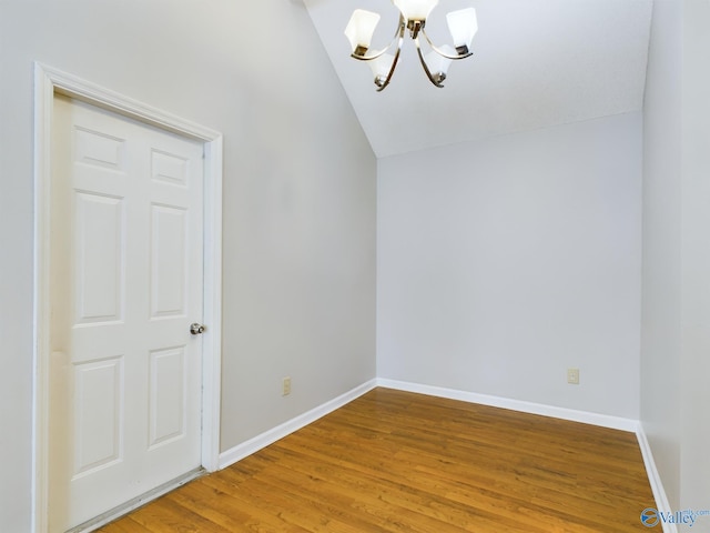 spare room with a chandelier, vaulted ceiling, and hardwood / wood-style flooring