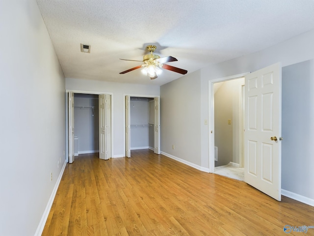 unfurnished bedroom with a textured ceiling, light hardwood / wood-style floors, ceiling fan, and two closets