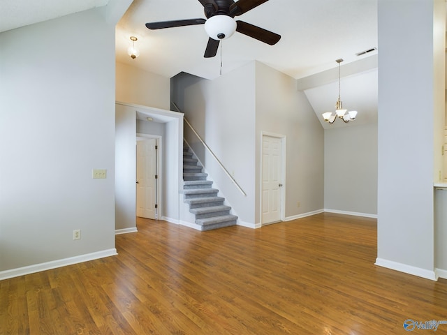 unfurnished living room with hardwood / wood-style flooring, ceiling fan with notable chandelier, and vaulted ceiling