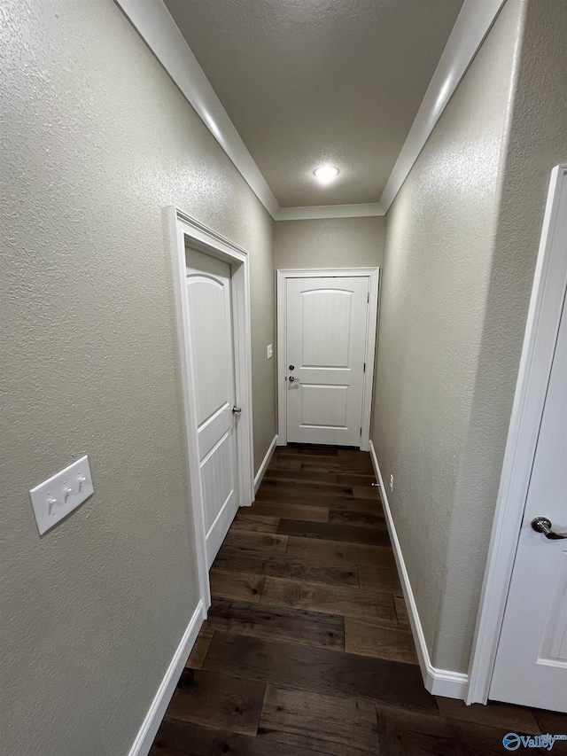 hall featuring ornamental molding, baseboards, dark wood finished floors, and a textured wall