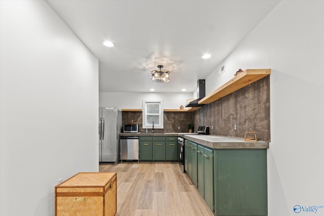 kitchen with backsplash, appliances with stainless steel finishes, light wood-type flooring, wall chimney exhaust hood, and green cabinets