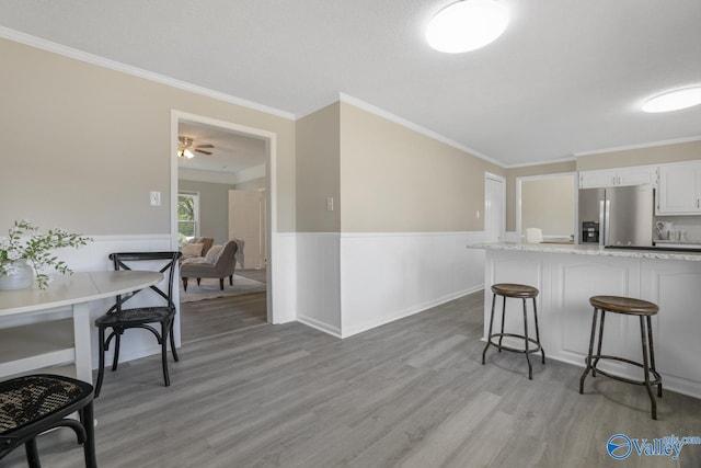 1816 Devonshire Dr SE, Decatur, AL 35601 - kitchen featuring stainless steel fridge with ice dispenser, a kitchen breakfast bar, light wood-type flooring, wainscoting, and white cabinets