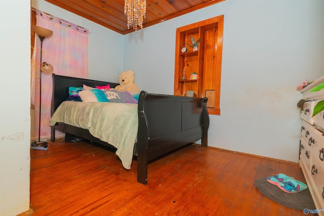 bedroom featuring a chandelier, hardwood / wood-style floors, wood ceiling, and ornamental molding