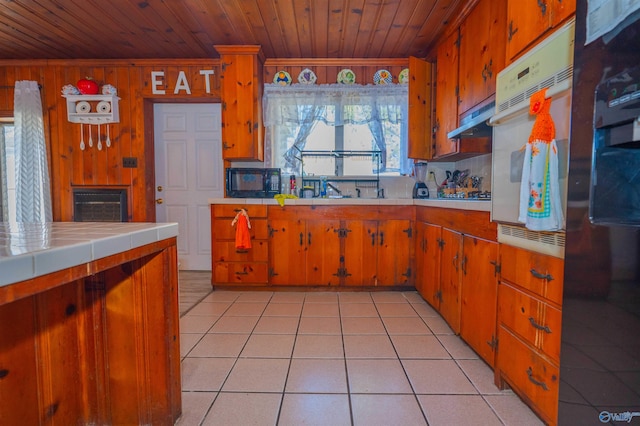 kitchen featuring black appliances, wood walls, tile counters, and wooden ceiling