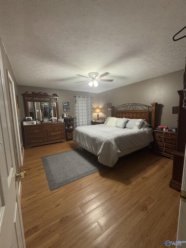 bedroom with a textured ceiling, wood-type flooring, and ceiling fan