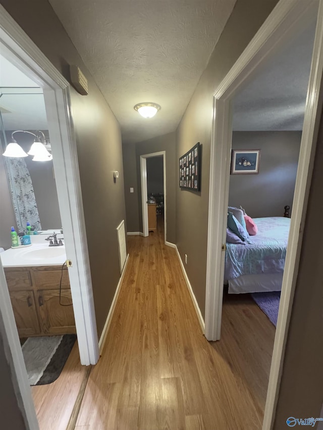 hall featuring sink, a textured ceiling, and light wood-type flooring