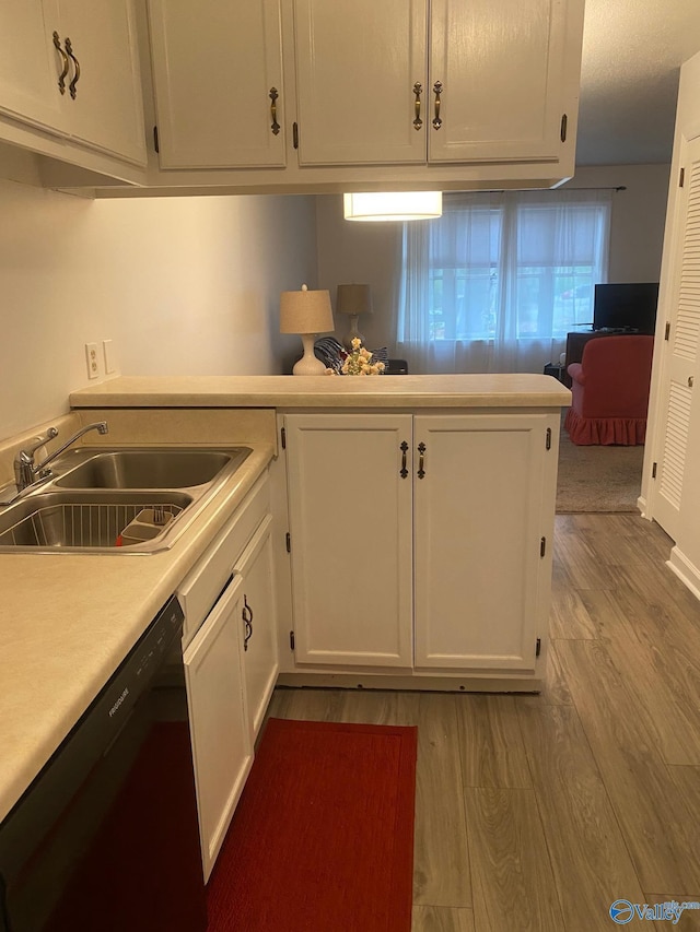 kitchen with light countertops, a sink, wood finished floors, dishwashing machine, and white cabinets