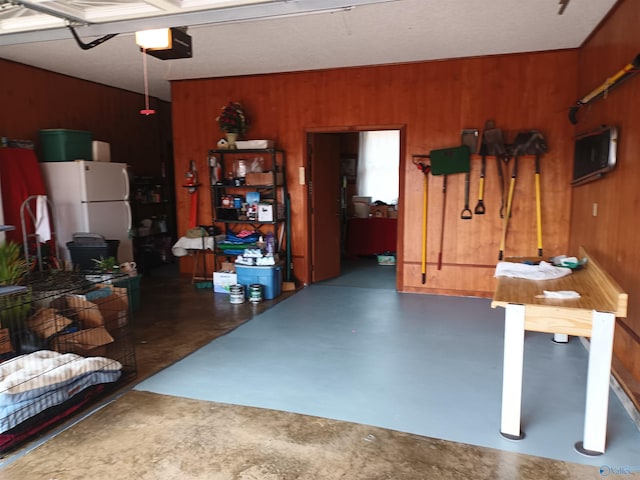 garage with a garage door opener, white fridge, and wood walls