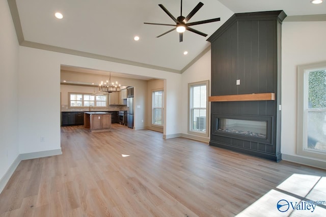 unfurnished living room featuring sink, high vaulted ceiling, a large fireplace, ceiling fan with notable chandelier, and light wood-type flooring