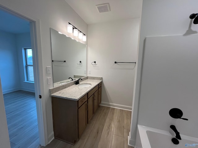 bathroom with a tub to relax in, vanity, and wood-type flooring