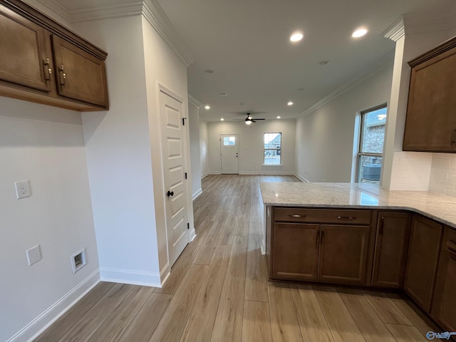 kitchen with ceiling fan, light stone counters, kitchen peninsula, and crown molding