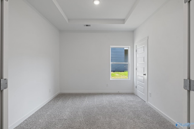 carpeted empty room with visible vents, baseboards, and a raised ceiling