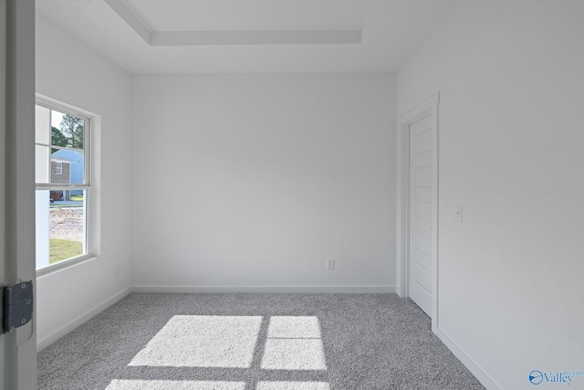 carpeted empty room featuring a tray ceiling and baseboards