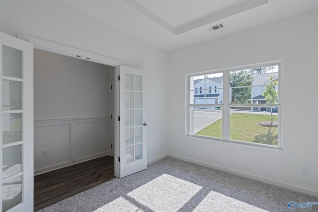 carpeted empty room with french doors, a raised ceiling, visible vents, and a decorative wall