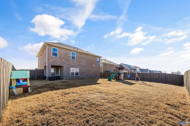 back of house featuring brick siding, a lawn, a playground, and a fenced backyard