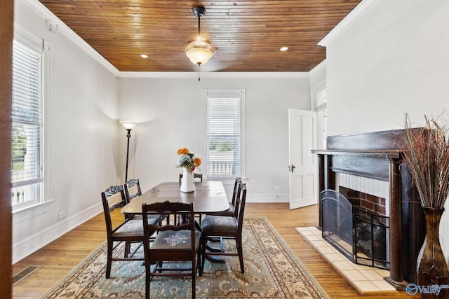 dining area featuring a tiled fireplace, light hardwood / wood-style flooring, and ornamental molding