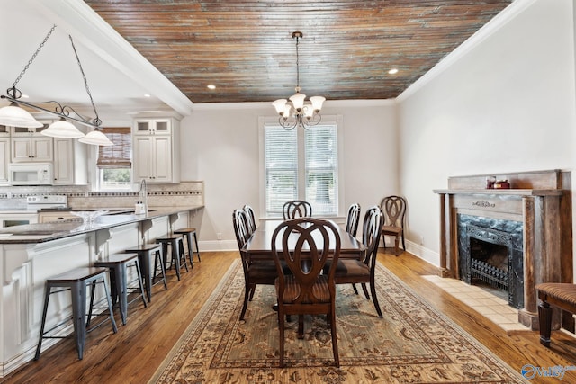 dining area featuring sink, a notable chandelier, crown molding, wood-type flooring, and a tiled fireplace