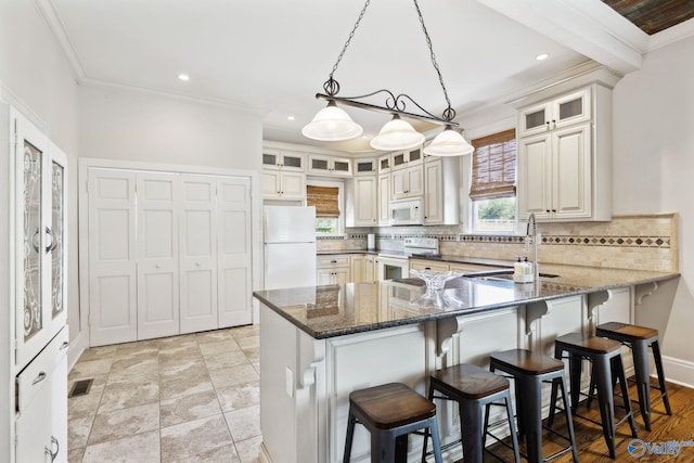 kitchen with dark stone counters, white appliances, crown molding, sink, and decorative light fixtures