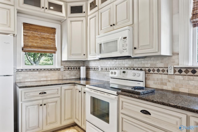 kitchen featuring cream cabinets, dark stone counters, and white appliances