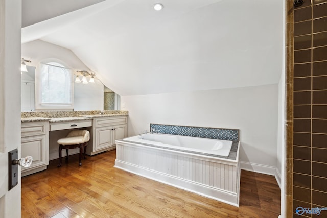 bathroom featuring vanity, hardwood / wood-style flooring, vaulted ceiling, and a bathtub