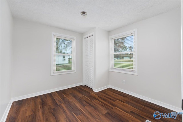 spare room featuring a textured ceiling, a healthy amount of sunlight, and dark hardwood / wood-style floors