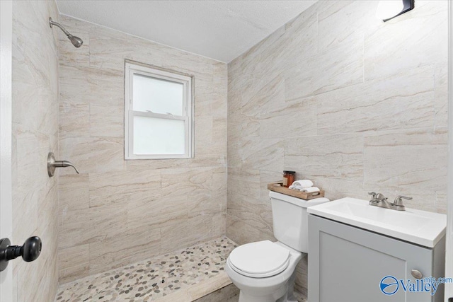 bathroom featuring a textured ceiling, a tile shower, vanity, toilet, and tile walls