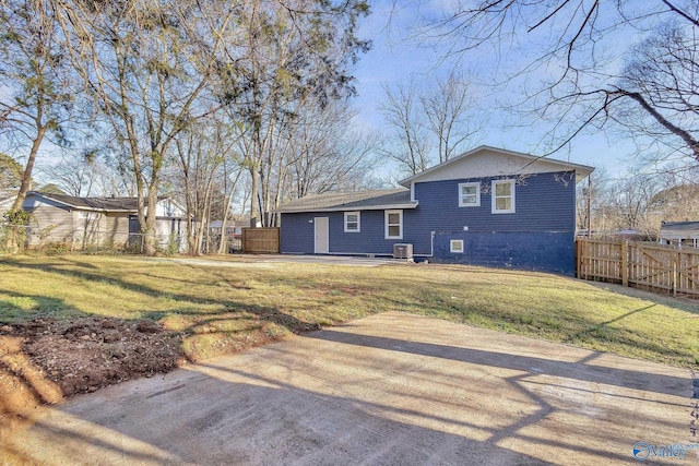 rear view of house with cooling unit, fence, and a lawn