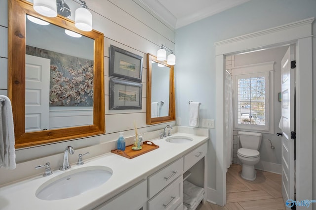 full bathroom featuring double vanity, toilet, crown molding, and a sink