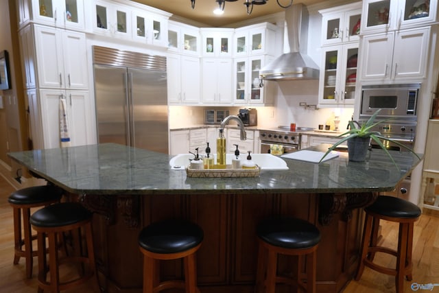 kitchen with built in appliances, white cabinetry, and wall chimney range hood