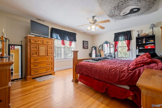 bedroom featuring multiple windows, ceiling fan, light hardwood / wood-style flooring, and a textured ceiling