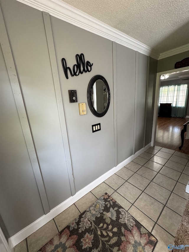 hall featuring a decorative wall, light tile patterned floors, a textured ceiling, and crown molding
