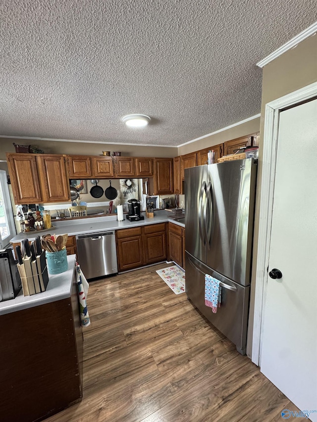 kitchen with brown cabinetry, a textured ceiling, crown molding, and appliances with stainless steel finishes