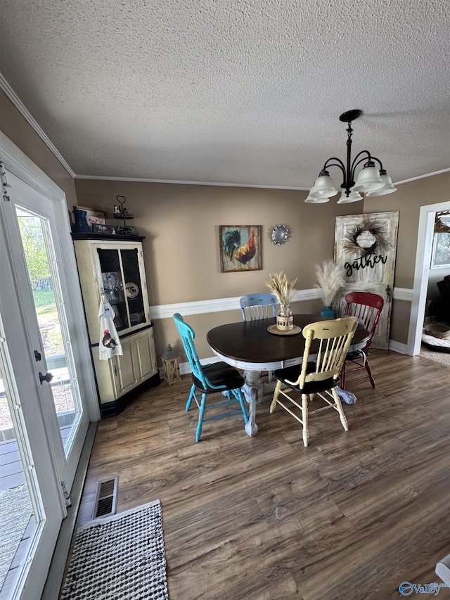 dining room with crown molding, dark wood finished floors, a textured ceiling, visible vents, and a notable chandelier