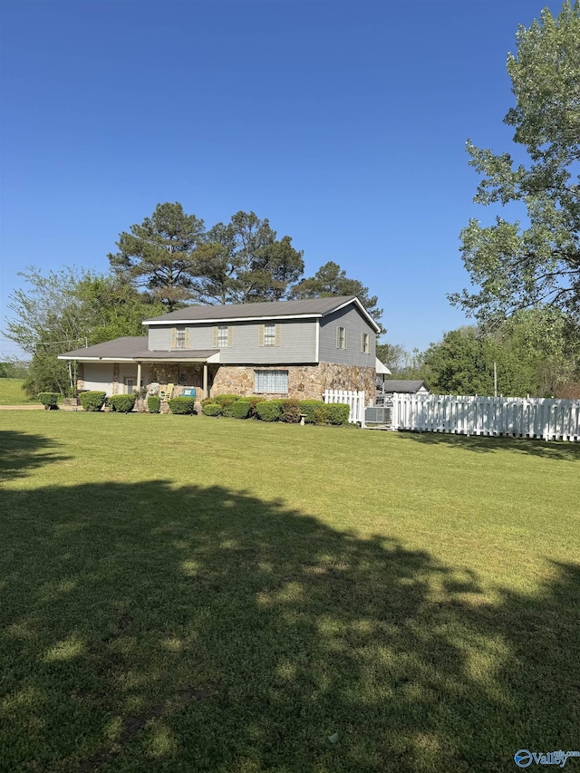 rear view of property with central AC unit, fence, stone siding, and a lawn