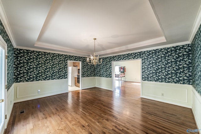 unfurnished dining area featuring a raised ceiling, wood-type flooring, ornamental molding, and a chandelier