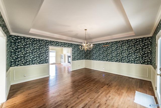 empty room with hardwood / wood-style floors, a tray ceiling, and a chandelier