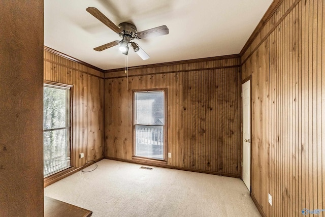 carpeted empty room with crown molding, ceiling fan, and wooden walls