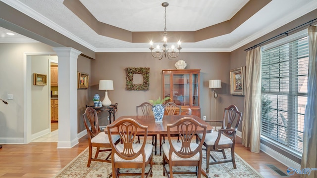 dining area featuring a raised ceiling, light wood-type flooring, ornate columns, and a chandelier